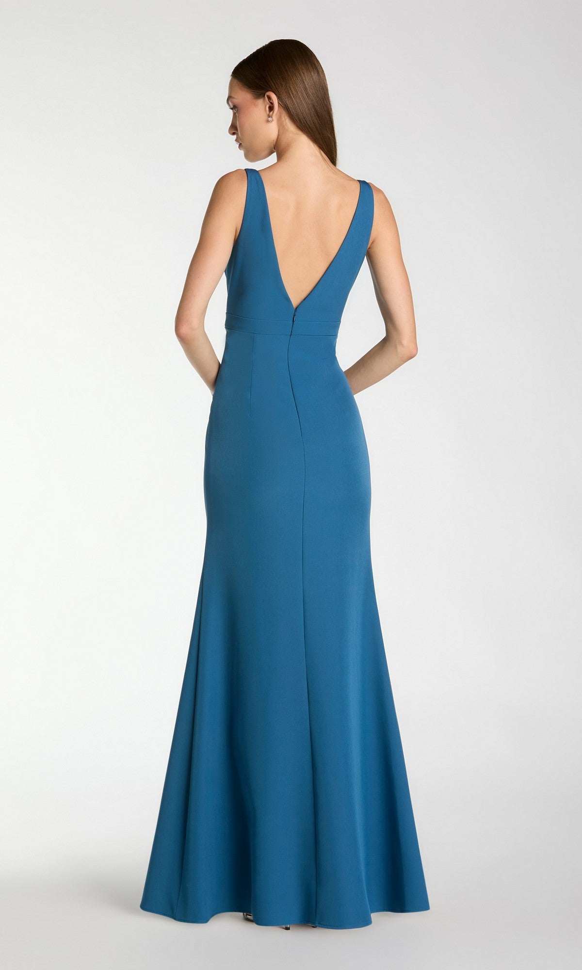 A woman in the Mac Duggal 2371 long formal dress, a sleeveless teal crepe evening gown with a deep V-back, stands facing away against a plain light background.
